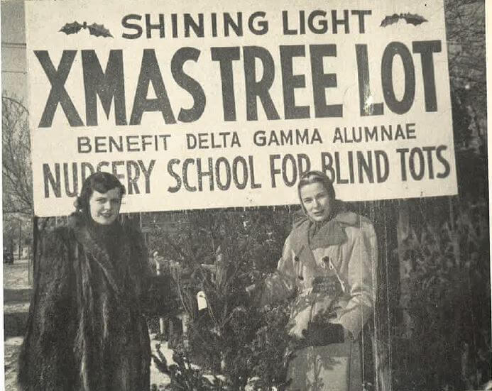 Photo of the first Shining Light Tree lot in 1951, showing two women in elegant fur coats in the holiday tree lot.
